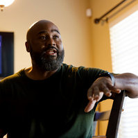 Bald African American man sits in a chair. 
