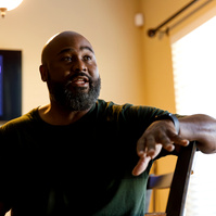 Bald African American man sits in a chair. 