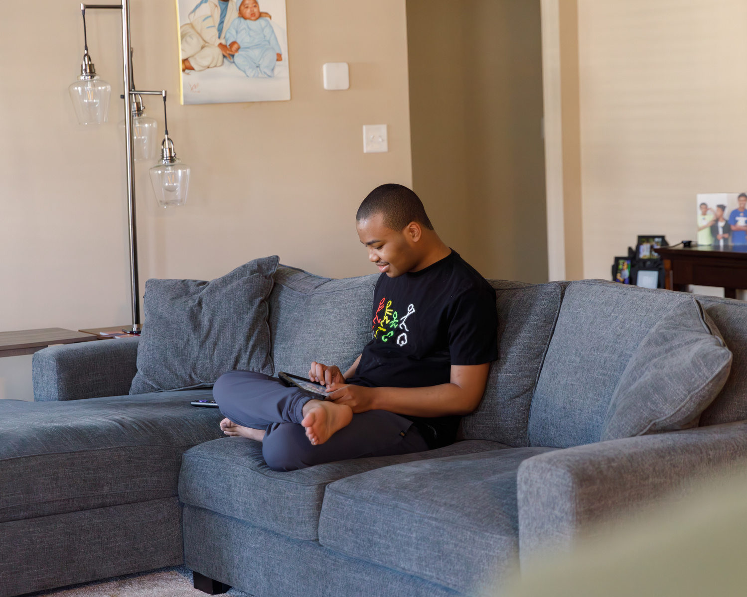 A young African American man sits on a blue sofa and looks at a cell phone