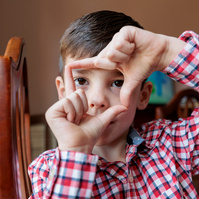 A small boy in a plaid shirt makes a square shape with his hands