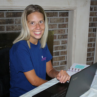 A blond woman sits in front of a laptop computer and smiles for the camera.