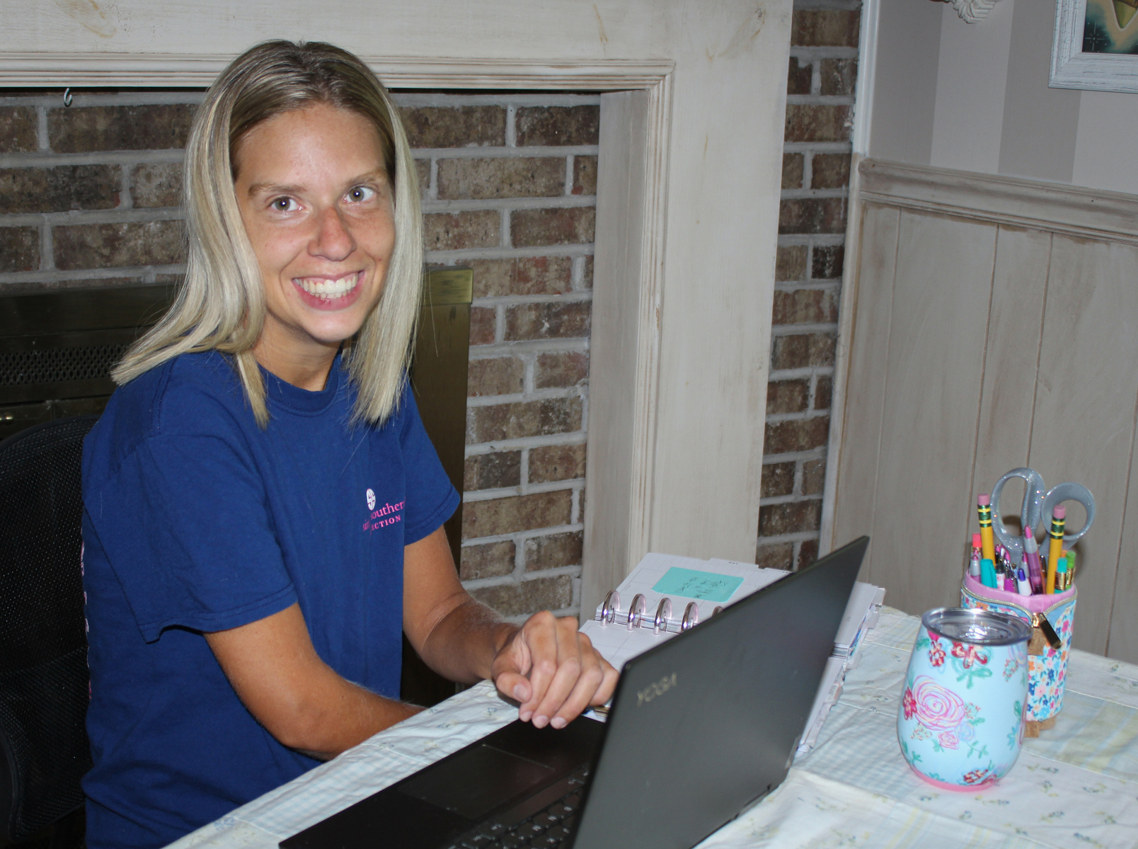 A blond woman sits in front of a laptop computer and smiles for the camera.