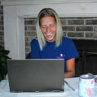 A blond woman sits in front of a laptop computer.  