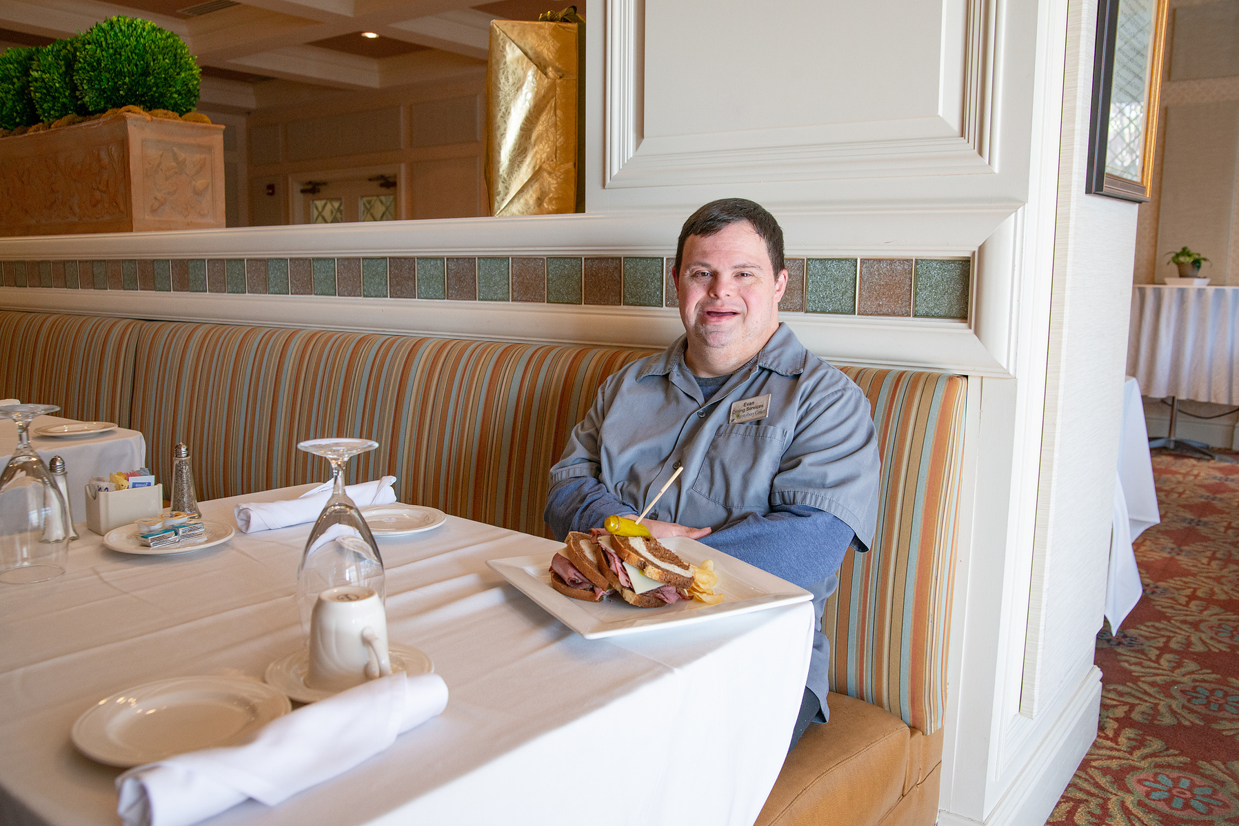 A young man in a grey shirt sits in a dining room at a table. 
