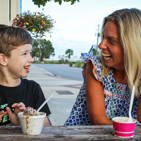 A blond woman and a little boy sit at a table and eat ice cream. 
