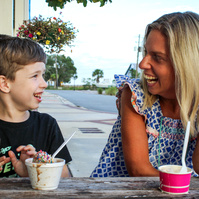 A blond woman and a little boy sit at a table and eat ice cream. 