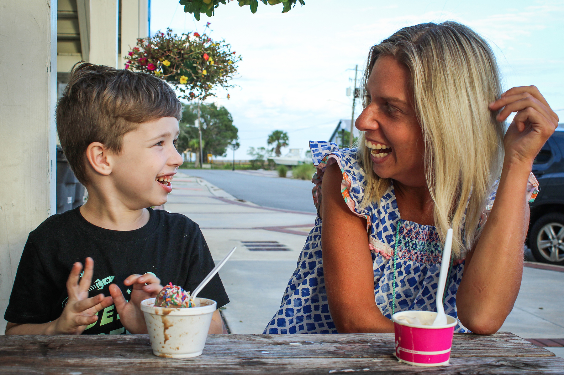 A blond woman and a little boy sit at a table and eat ice cream. 