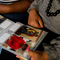 Two women sit on a sofa and look through a photo album. 