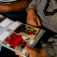 Two women sit on a sofa and look through a photo album. 