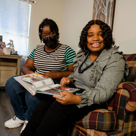 Two women sit close together on a sofa inside a home. 