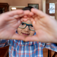 Small boy in a plaid shirt and glasses makes a square shape with his hands