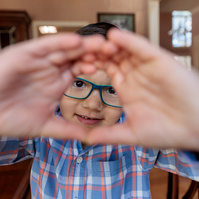 Small boy in a plaid shirt and glasses makes a square shape with his hands