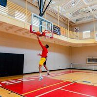 A man wears a bright red shirt while playing basketball in a gymnasium. 