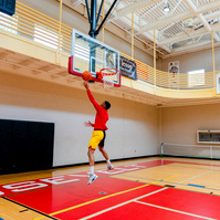 A man wears a bright red shirt while playing basketball in a gymnasium. 