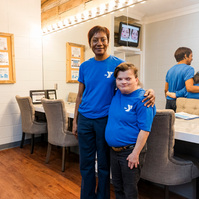 Two women wear matching blue t-shirts and stand in front of a theatre dressing room. 