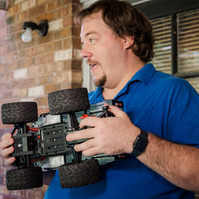 A man in a blue polo shirt holds a remote-controlled truck. 
