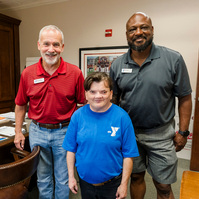 Three YMCA employees stand in an office and smile for the camera. 