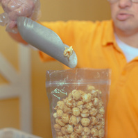 Man in yellow shirt uses a metal scoop to fill a bag full of popcorn.