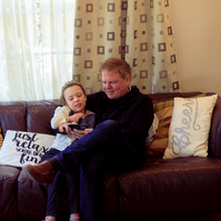 A young girl and her father sit on a sofa and look at a smartphone. 