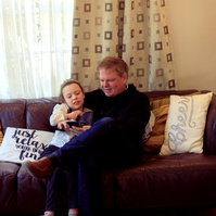 A young girl and her father sit on a sofa and look at a smartphone. 