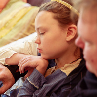 A young girl and her father sit on a sofa and look at a smartphone. 