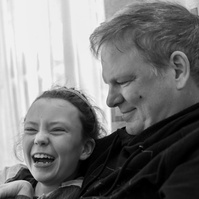 A young girl laughs as her father looks at her smiling. 