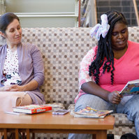 Mother and daughter sit on a patterned sofa and enjoy books.