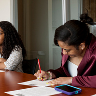 Two African American female college students sit at a conference table and work. 