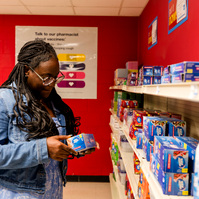 Young African American woman wears braids and looks at items on a shelf in a mock drug store. 