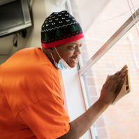 A man in an orange shirt, blue knit cap and white facemask cleans a window. 