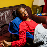 A young African American man wears a red shirt and sits in a wheelchair.
