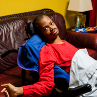 A young African American man wears a red shirt and sits in a wheelchair.