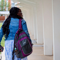 Young African American woman wears braids and walks down a walkway.