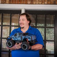 A man in a blue polo shirt holds a remote-controlled truck. 