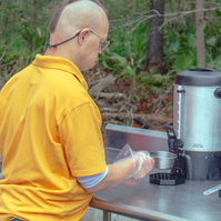 Man in yellow shirt pours a cup of coffee from a steel coffee pot.