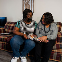 Two women sit close together on a sofa inside a home. 