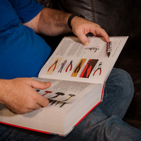 A man in a blue polo shirt looks at a book that explains tools needed for car repair. 