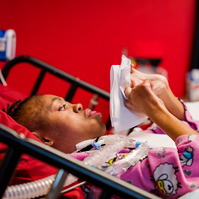 A young African American woman lies in a bed and folds paper. 