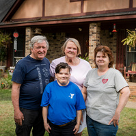 A family stands in front of a home and smiles for the camera.