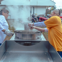 Two people dump popcorn from a steaming metal machine.