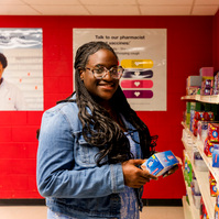 Young African American woman wears braids and looks at items on a shelf in a mock drug store. 