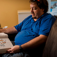 A man in a blue polo shirt looks at a book. 