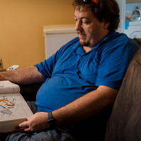 A man in a blue polo shirt looks at a book. 
