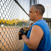 Man stands at fa ence with baseball glove.