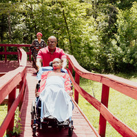 A father pushes his son in a wheelchair as his wife follows them on a red walkway. 