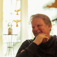 A middle aged man sits in front of a sun filled window. 