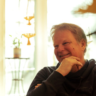 A middle aged man sits in front of a sun filled window. 