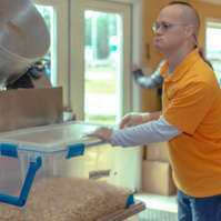 Man wears a yellow shirt as he places a clear bin on a table.