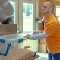 Man wears a yellow shirt as he places a clear bin on a table.