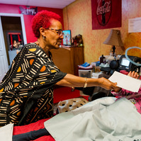 A woman with red hair hands her daughter a sheet of paper as she lies in bed. 